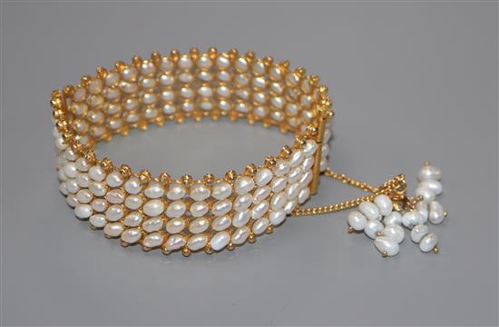 An Indian? yellow metal and baroque pearl set hinged bangle, with pearl set tassle safety chain.